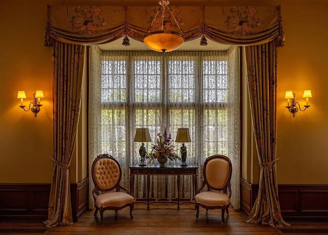 Two armchairs facing a large window, warm light from wall lamps
