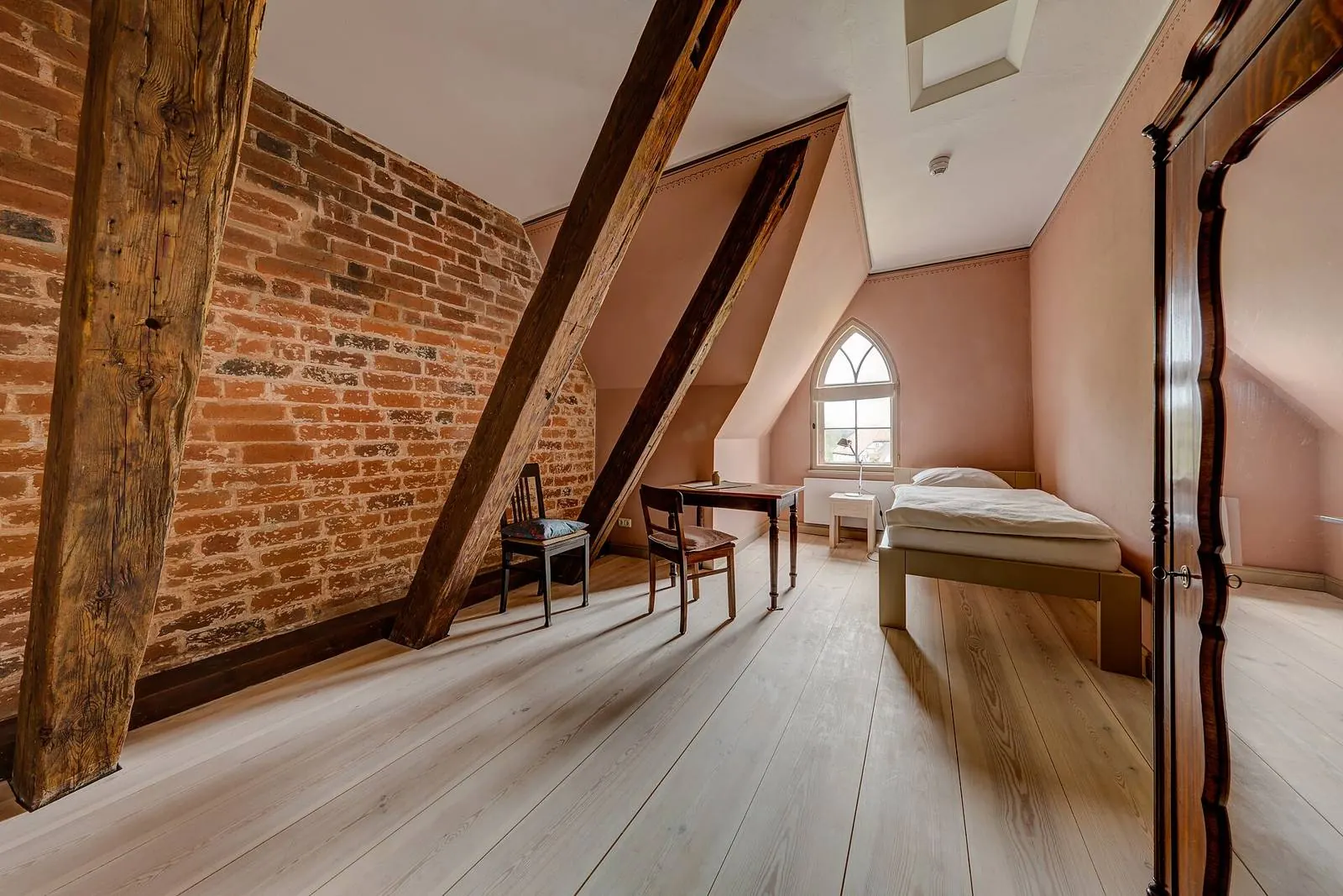 Attic bedroom with exposed beams, brick wall and pale floorboards