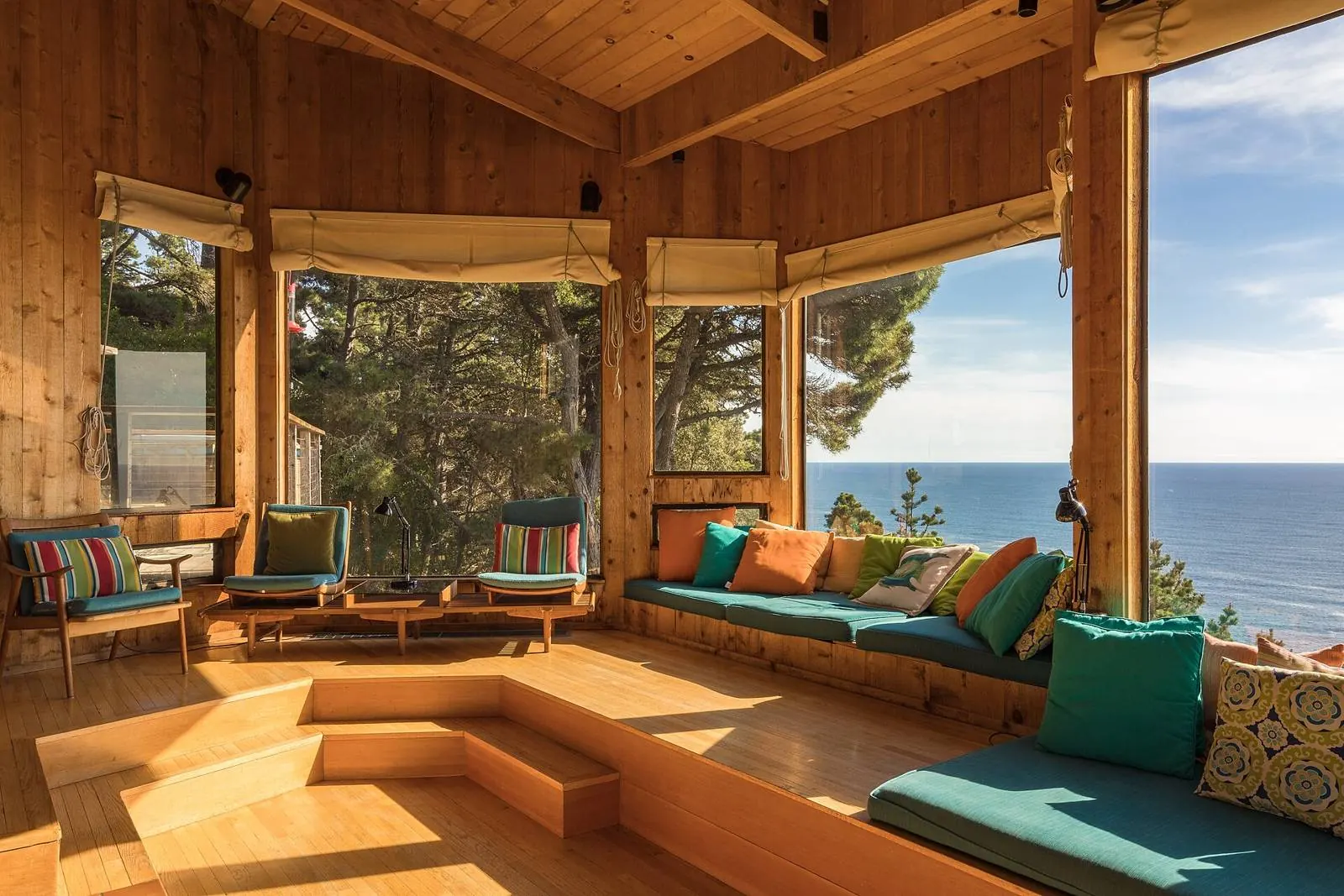 Light wood living room with a window seat beneath a large opening onto the ocean